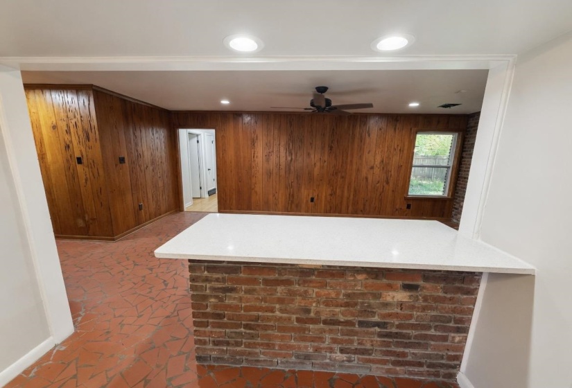 Exposed brick half-wall with a white countertop, wood paneling, recessed lighting, and a ceiling fan