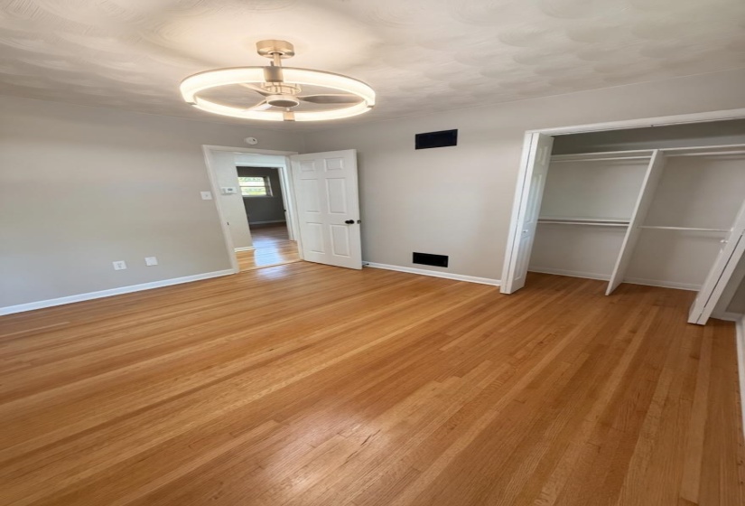 Bright interior space featuring wood-finish flooring, a modern ceiling fan with integrated lighting, a built-in closet with shelving, and light neutral wall tones