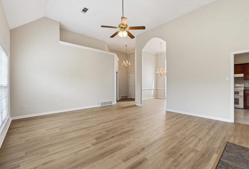 Spacious living area featuring vaulted ceilings, wood-finish flooring, a ceiling fan with integrated lighting, and an arched entryway