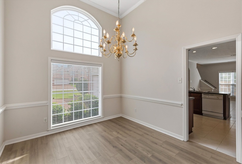 Dining area featuring a soaring ceiling, an arched window, a brass-finish chandelier, wood-finish flooring, and white trim molding