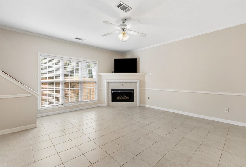 Spacious room featuring neutral tile flooring, a fireplace with a mantel, and a multi-pane window with blinds