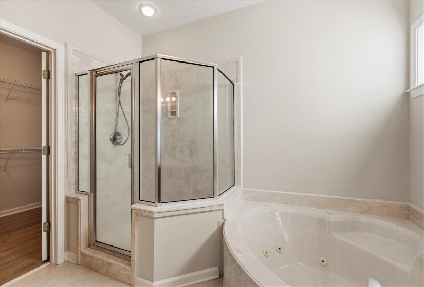 Jetted soaking tub with tile surround, glass-enclosed shower, recessed lighting, and tile flooring
