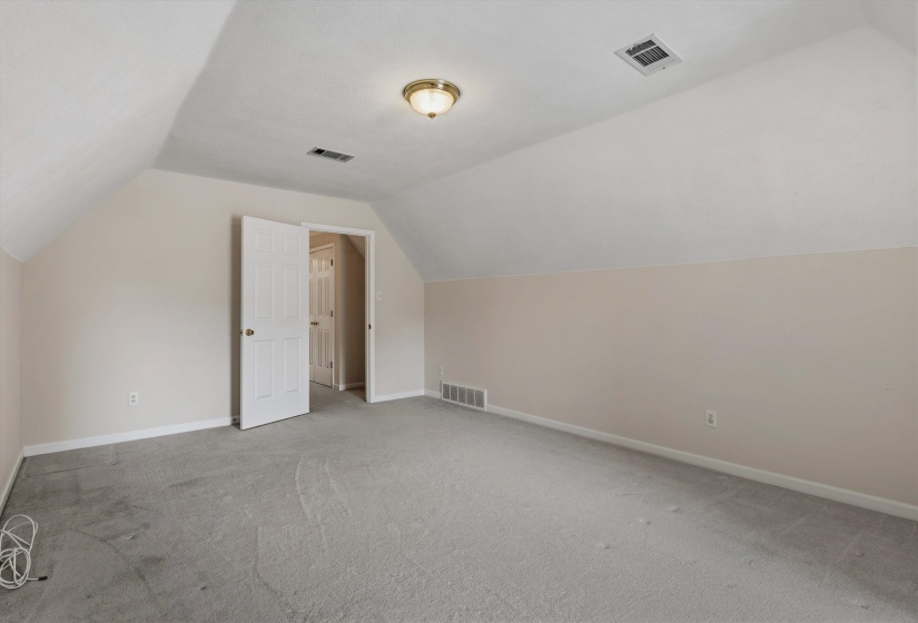 Carpeted room with a vaulted ceiling, ceiling-mounted light fixture, and neutral-toned walls
