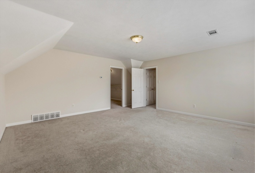 Spacious room featuring neutral carpeting, light-toned walls, and sloped ceiling details