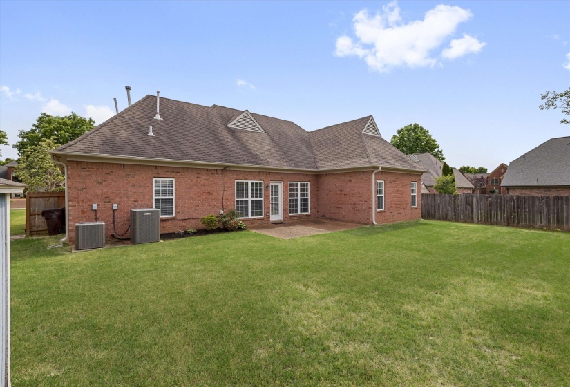 Brick exterior featuring a gabled roofline, multiple windows, a rear patio, and a spacious lawn