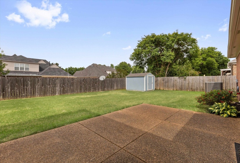 Expansive backyard featuring a concrete patio, a manicured lawn, a privacy fence, a storage shed, and mature trees