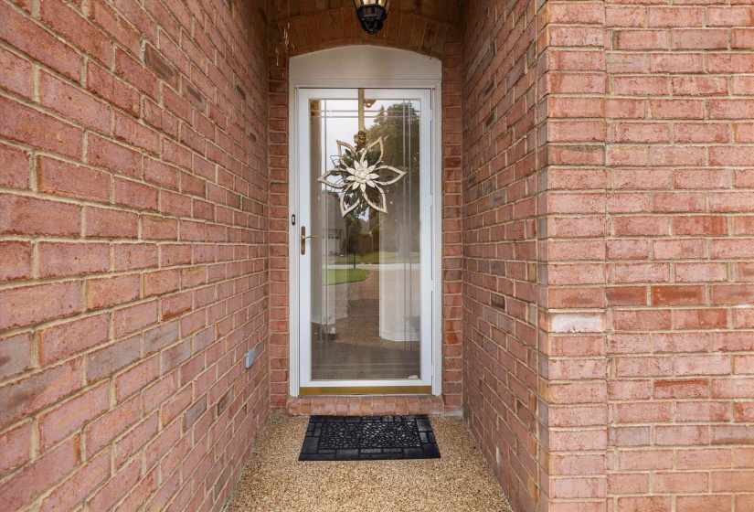 Red brick facade featuring a white storm door with glass panels and an arched entryway