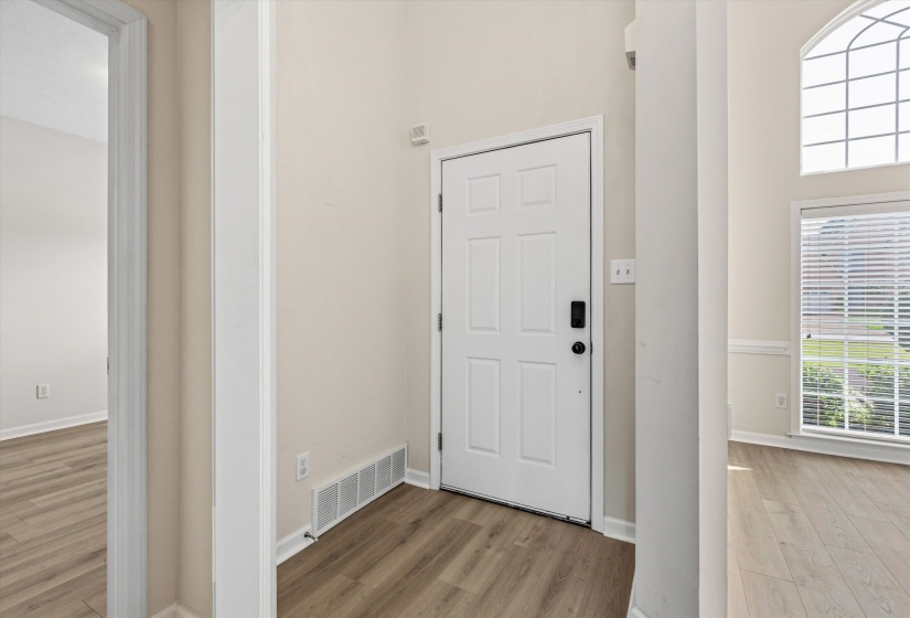 Entryway featuring light wood-finish flooring, a white paneled door with modern hardware, and a high arched window above a rectangular window with blinds