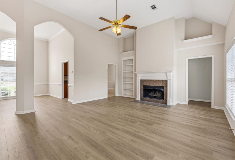 Spacious living area featuring vaulted ceilings, wood-finish flooring, a fireplace with a stone surround and mantle, and built-in shelving