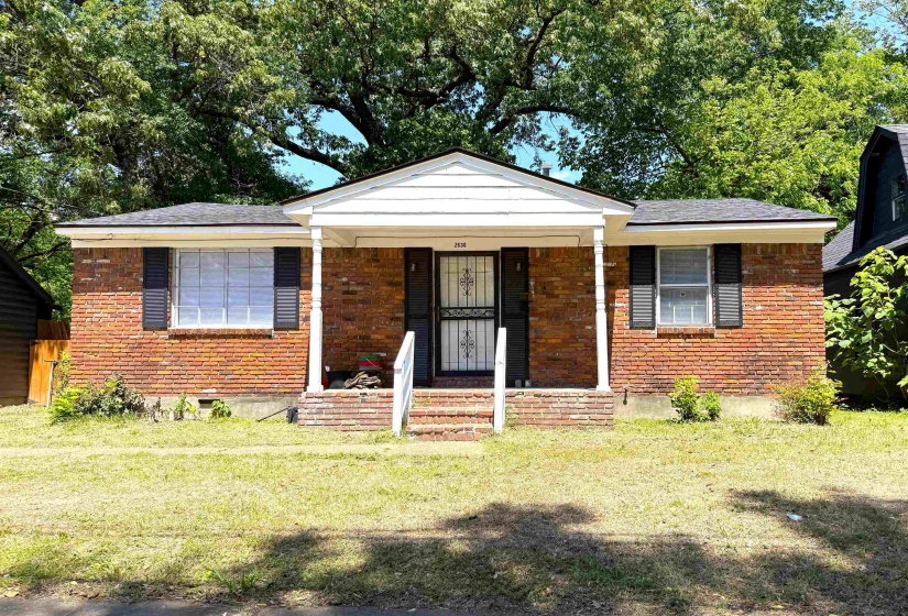 Brick facade with black shutters, covered entry porch, white columns, and a front lawn