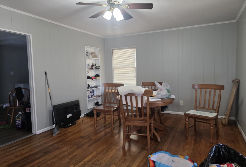 Dining area featuring wood-finish flooring, light gray vertical plank walls, white ceiling trim, and a ceiling fan with integrated lighting