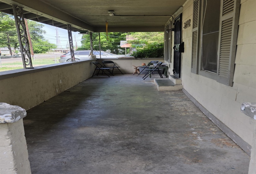 Covered concrete front porch with decorative metal support columns and louvered window shutters