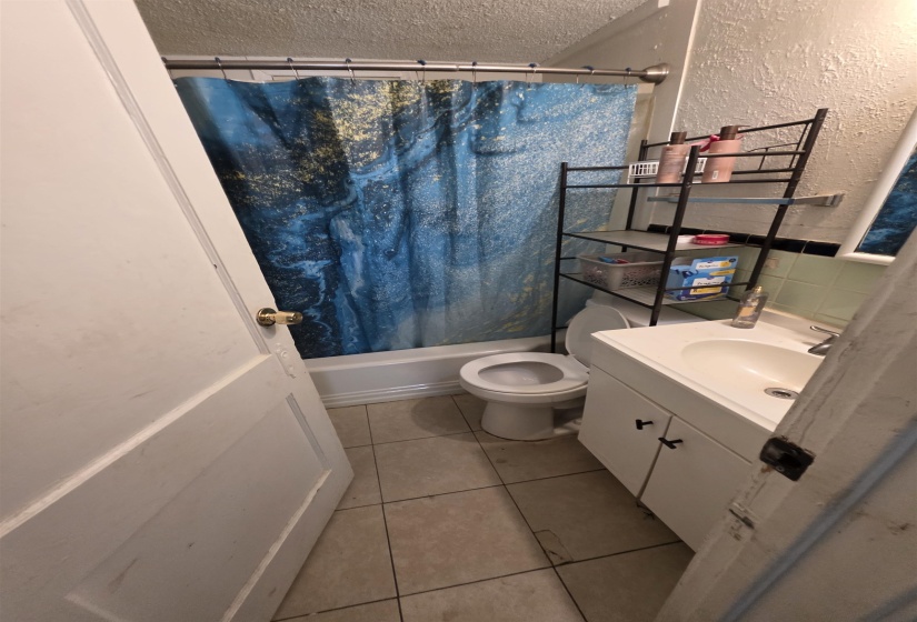 Bathroom featuring a built-in tub with shower, a white vanity with cabinet storage, a ceramic sink, and tile flooring