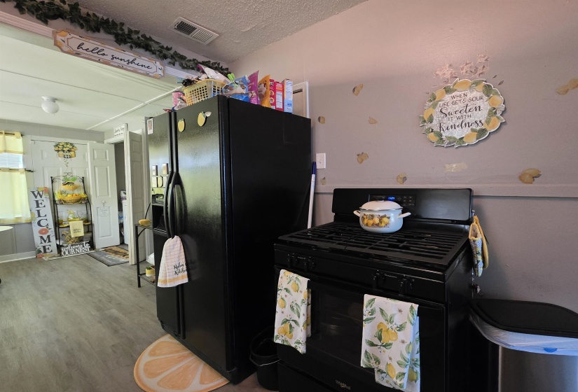 Black gas range with a matching black refrigerator, light gray wall, and wood-finish flooring