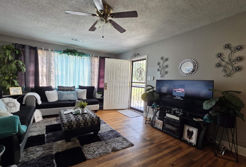 Living room featuring wood-finish flooring, a ceiling fan with integrated lighting, and multiple windows