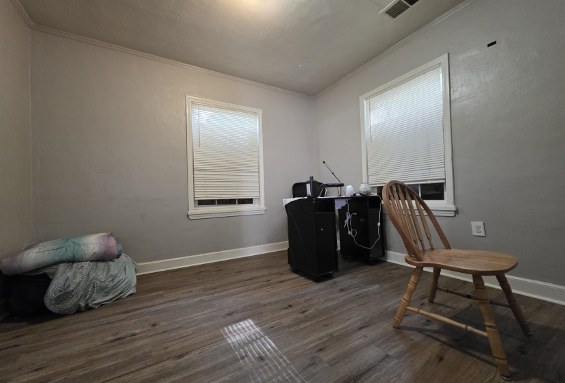 Room featuring two windows with blinds, crown molding, baseboards, and wood-finish flooring