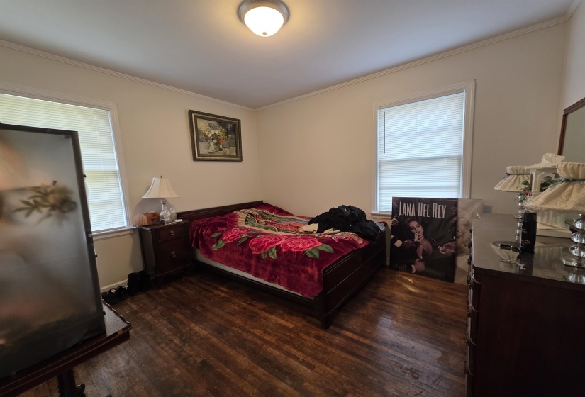 Spacious room featuring wood-finish flooring, two windows with blinds, a ceiling-mounted light fixture, and crown molding