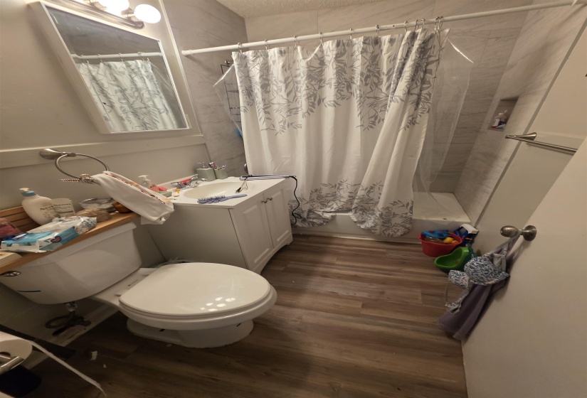 Bathroom featuring a white vanity with a single sink, an integrated shower/tub, and wood-finish flooring
