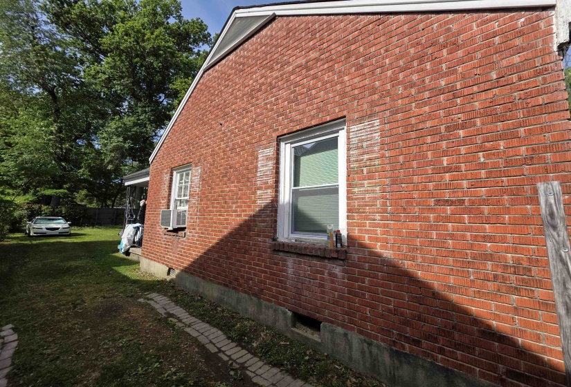 Red brick exterior featuring a white framed window and a window-mounted air conditioning unit
