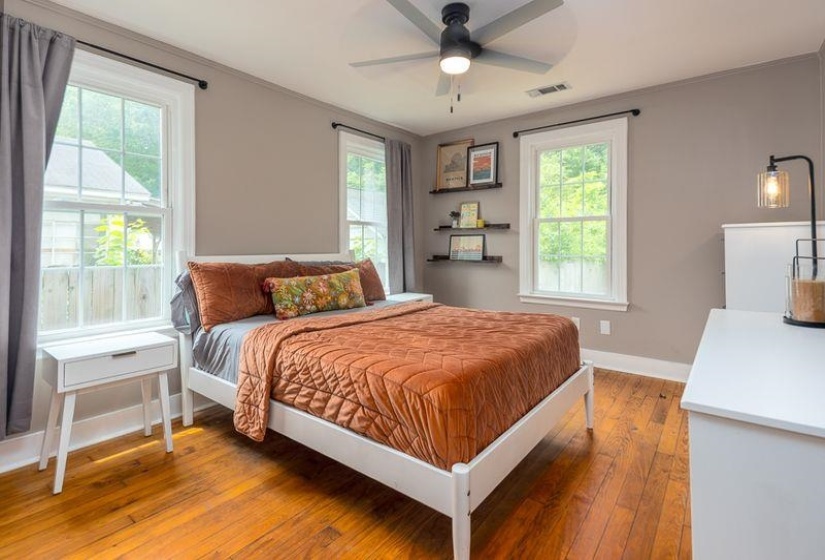 Hardwood flooring and neutral wall tones define this room, featuring a ceiling fan, two double-hung windows with white trim, and a built-in floating shelf unit