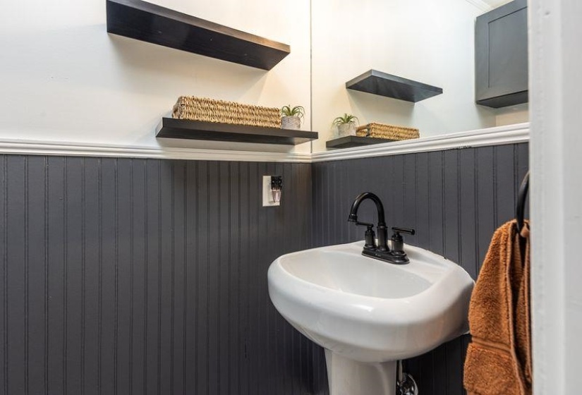 Pedestal sink with a matte black faucet, framed by dark gray beadboard paneling