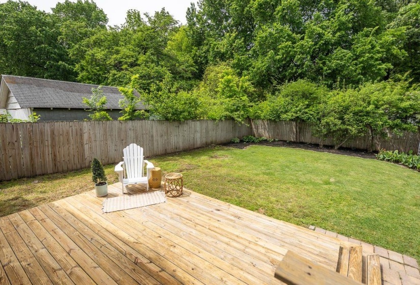 Spacious backyard featuring a wooden privacy fence, mature trees, and a tiered wooden deck