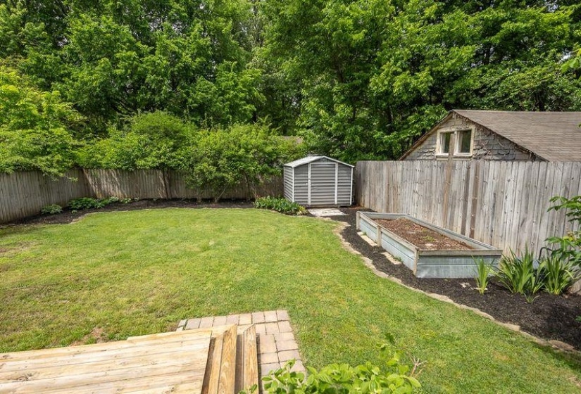 Expansive backyard with a manicured lawn, established privacy fencing, a storage shed, two elevated garden beds, and mature perimeter trees