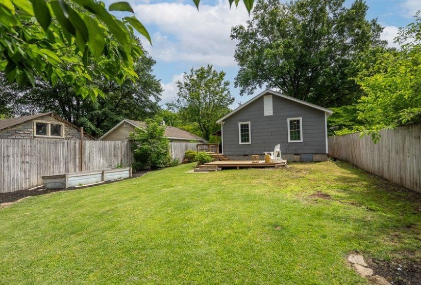 Expansive lawn with a wood privacy fence, a wooden deck, and a grey exterior home
