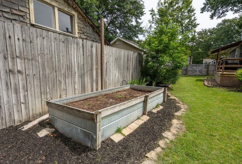 Expansive yard featuring a large raised garden bed, natural wood privacy fence, stone pathway, and manicured lawn
