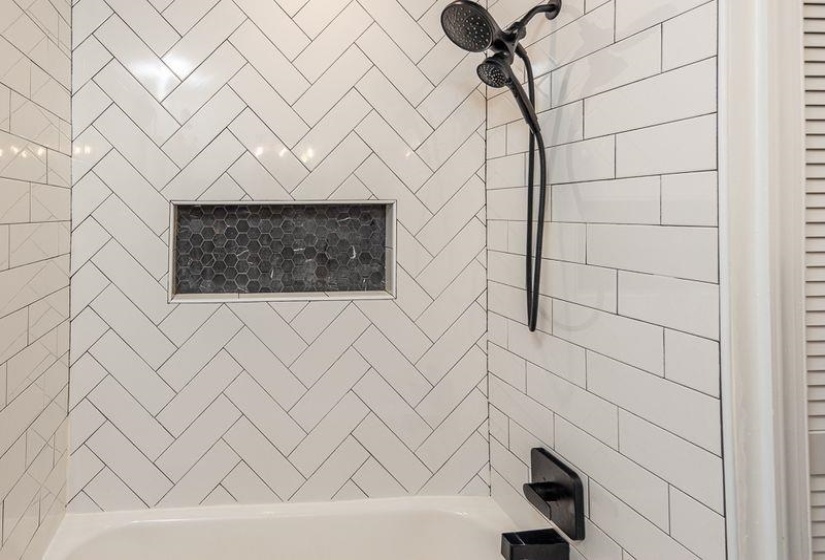 Herringbone-patterned subway tile shower surround with a built-in niche featuring dark hexagonal tile