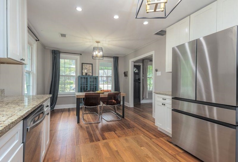 Kitchen and dining area featuring wood-finish flooring, white cabinetry, speckled granite countertops, and stainless steel appliances