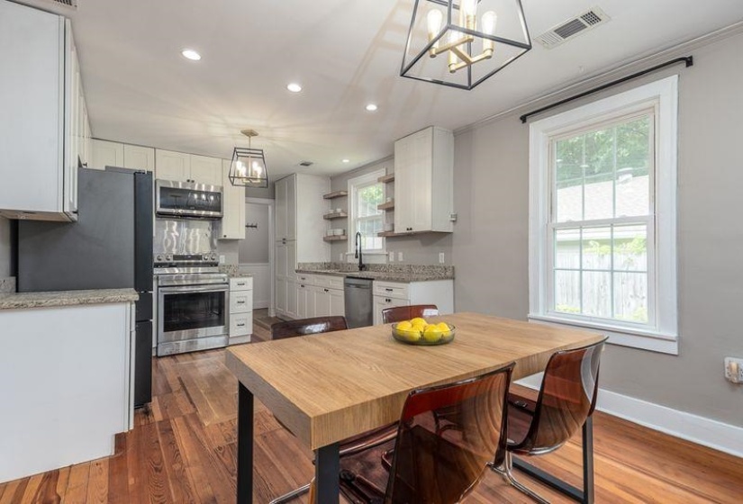 Open-concept kitchen and dining space featuring wood-finish flooring, white cabinetry, stainless steel appliances, recessed lighting, and a large window