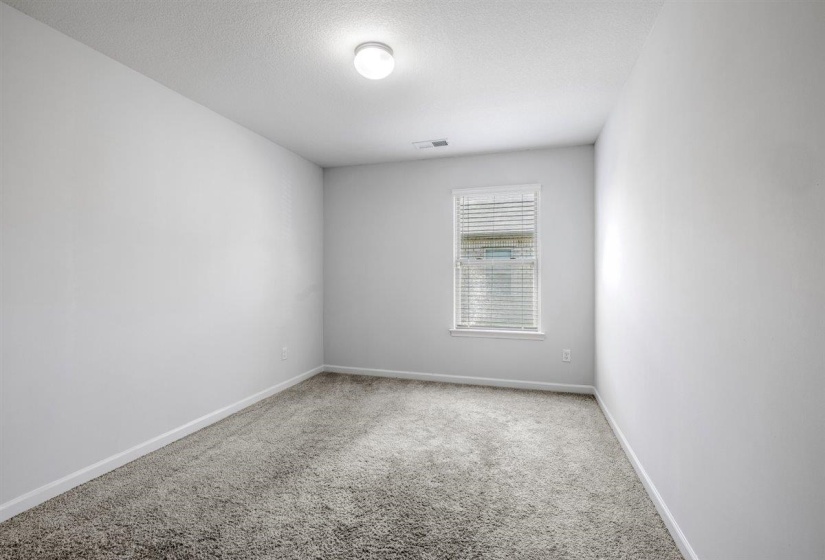 Neutral-toned room featuring light gray walls, textured carpeting, and white baseboards