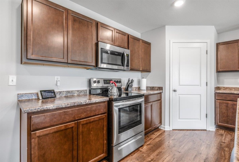 Kitchen featuring wood-finish flooring, dark wood cabinetry, speckled countertops, and stainless steel appliances including a range and built-in microwave
