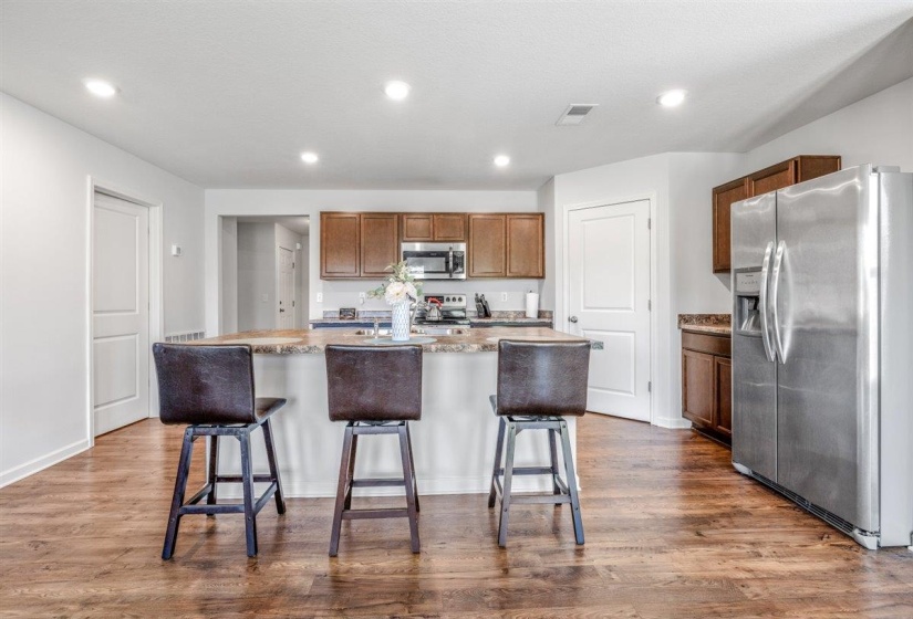 Kitchen featuring a spacious island with a stone-finish countertop, wood-finish flooring, recessed lighting, stainless steel appliances, and wood cabinetry