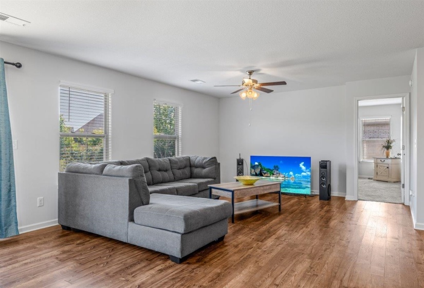Spacious living area featuring wood-finish flooring, white walls, and multiple windows with blinds