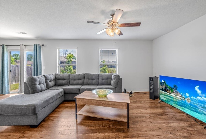 Living area with wood-finish flooring, white walls, and a ceiling fan with integrated lighting