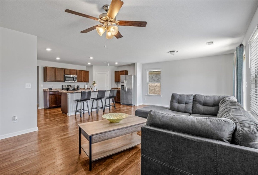 Open-concept living area featuring wood-finish flooring, a kitchen island with seating, dark wood cabinetry, stainless steel appliances, and recessed lighting