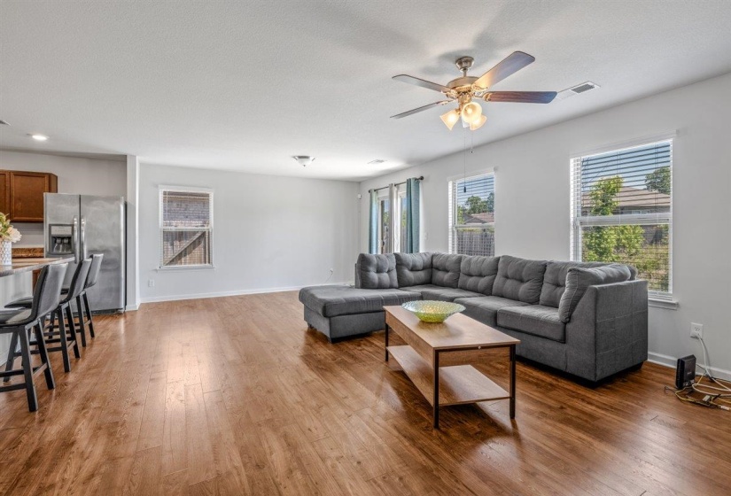 Open-concept living area featuring wood-finish flooring, multiple windows with blinds, and a ceiling fan with integrated lighting