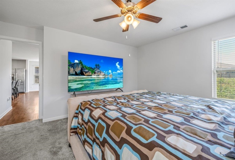 Bright room featuring soft gray carpeting, white painted walls, a flush-mounted ceiling fan with light kit, and a large window with horizontal blinds