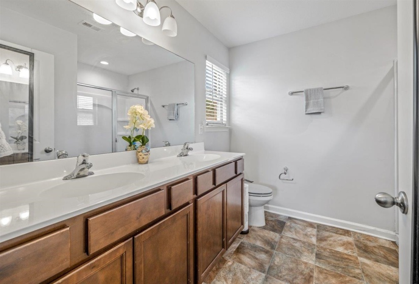 Bathroom featuring a double vanity with integrated sinks, wood-finish cabinetry, a large wall-mounted mirror, and a shower enclosure with a glass door