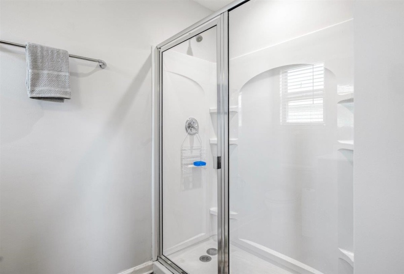 Clear glass shower enclosure with chrome frame, integrated shower shelving, and a bright white finish