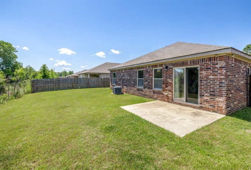 Expansive rear yard featuring a concrete patio, wood privacy fencing, and a brick exterior with sliding glass doors