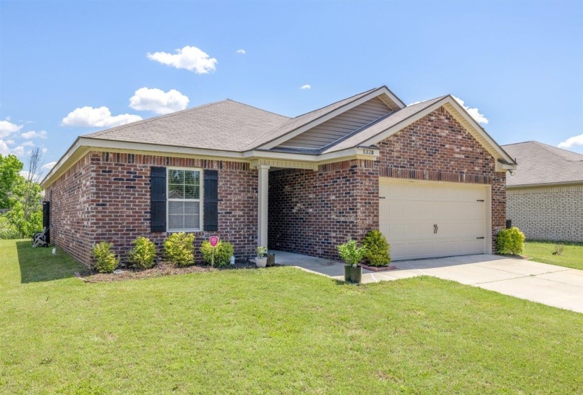 Brick exterior featuring a two-car garage with a light-colored door, a covered entryway with white columns, black window shutters, and a well-maintained front lawn