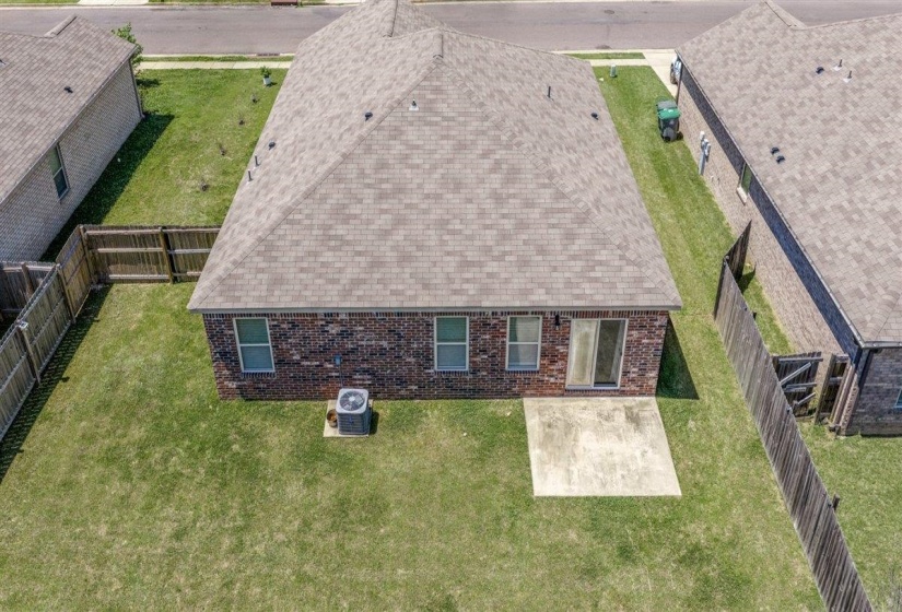 Rear exterior of a brick home featuring a pitched roof with asphalt shingles, a concrete patio, and a sliding glass door
