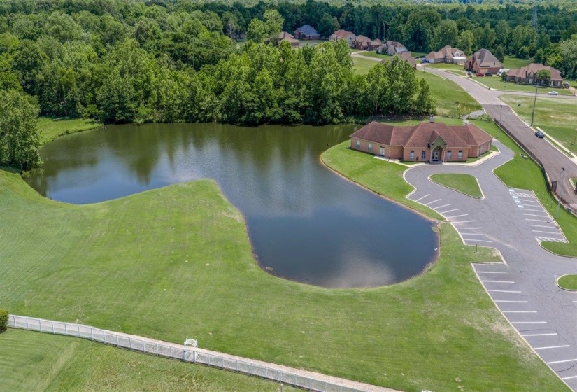 Expansive pond with surrounding green lawn and a brick building featuring a red shingle roof