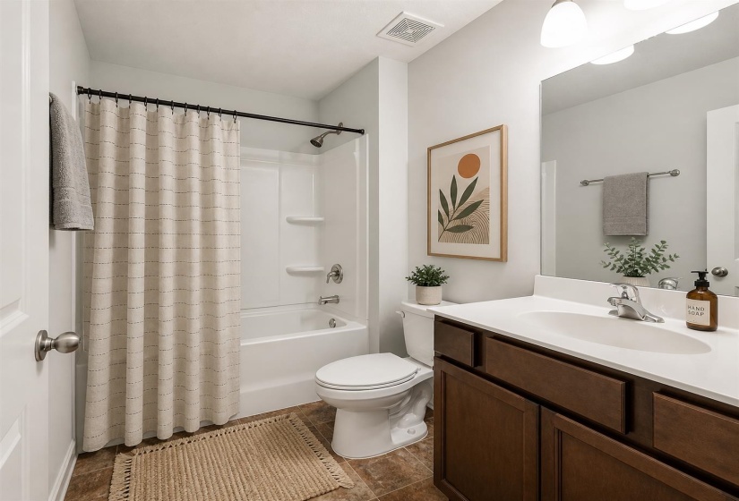Bathroom featuring a white tub/shower combination with a curved shower rod, a dark wood-finish vanity with a white countertop and integrated sink, a toilet, and brown-toned tile flooring