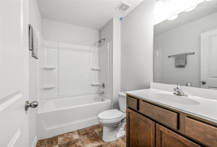 Bathroom featuring a white tub/shower combination, a vanity with a white countertop and wood-finish cabinetry, a large wall-mounted mirror, and tile flooring