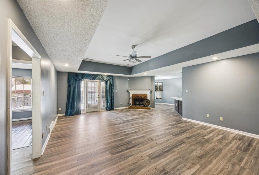 Open-concept living area featuring wood-finish flooring, a tray ceiling with a ceiling fan, and recessed lighting