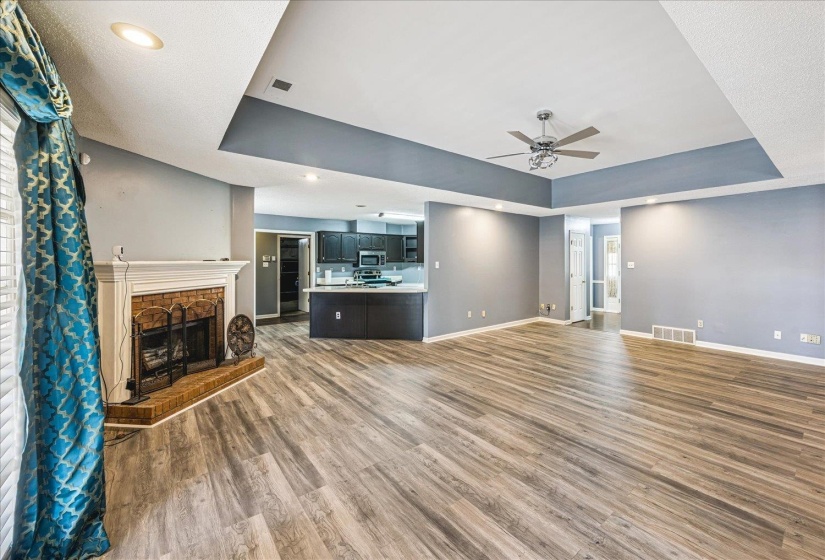 Expansive living space featuring wood-finish flooring and a tray ceiling with a ceiling fan